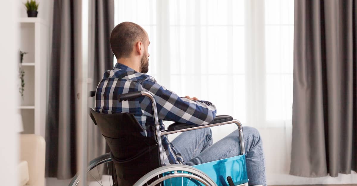 Man in a wheelchair, looking sadly out the window and dealing with the psychological effects of losing a limb